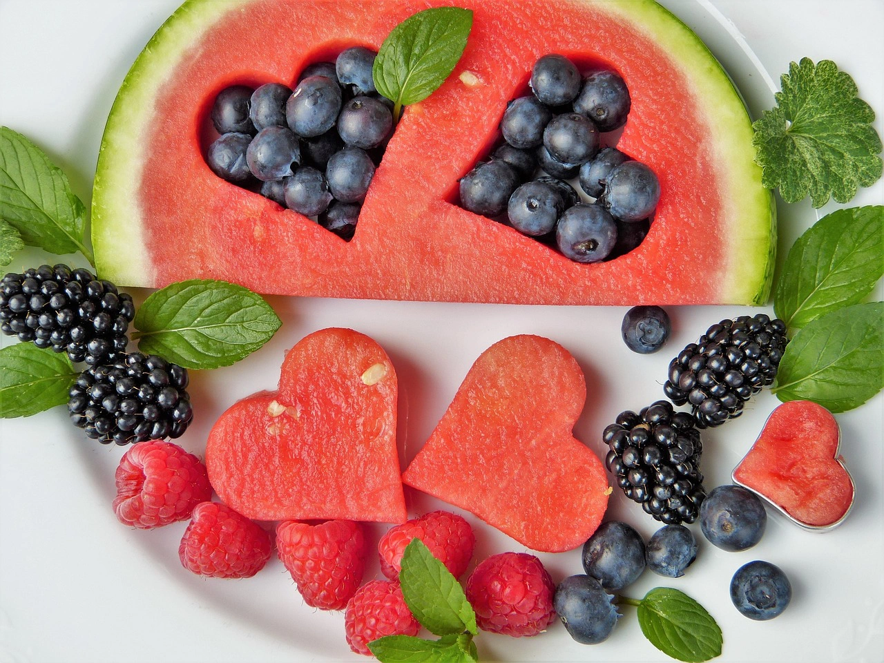 Melancia cortada em forma de corações com frutos vermelhos e hortelã